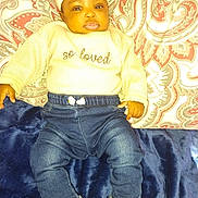 Tazori is registered to the contest to win money with this photo: baby, infant, headband, sweater, jeans, sneakers, blanket, cushion, patterned, fabric, clothing, person, lying_down, indoors, cute, young_child, face, expression, comfort, soft