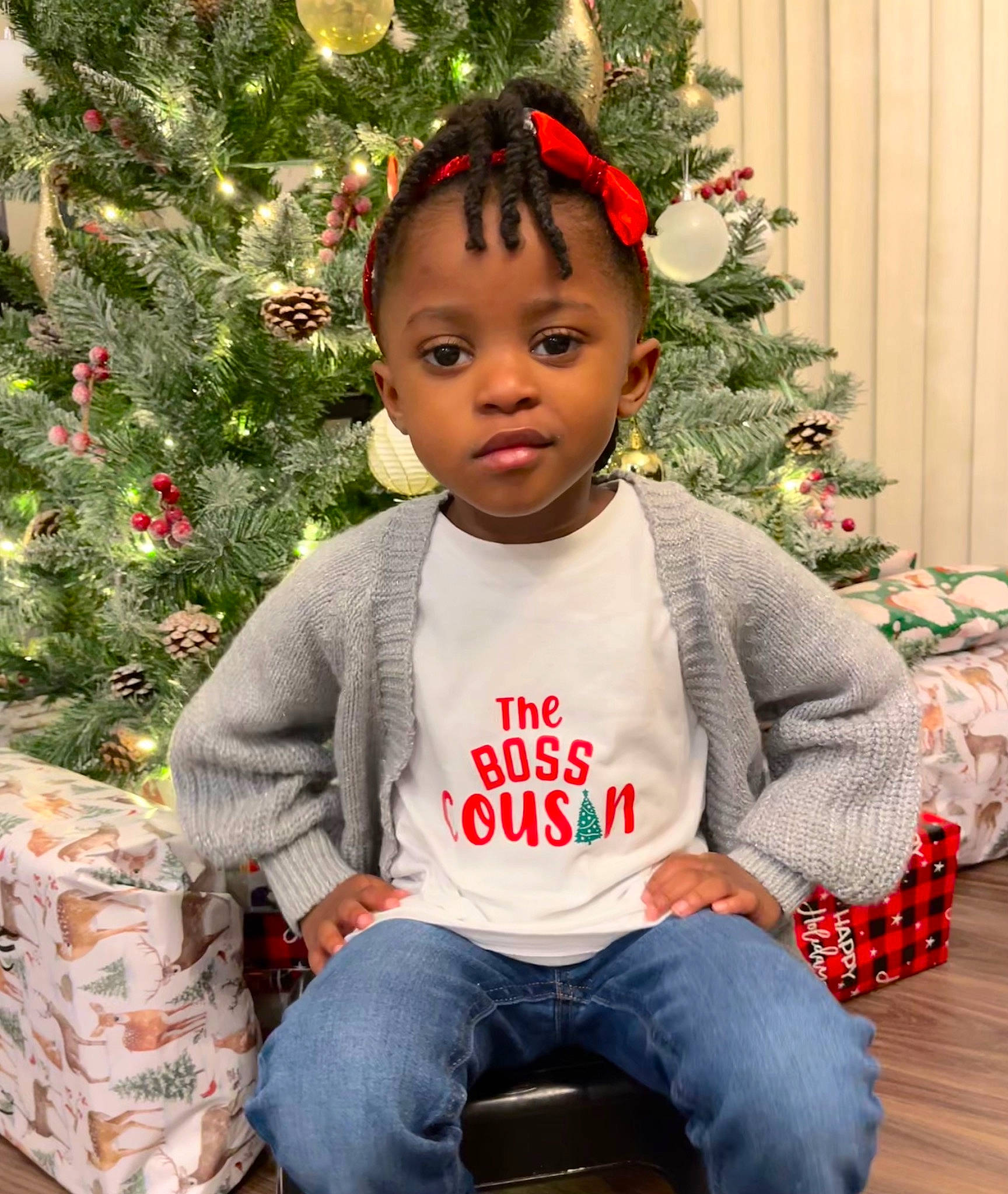 Janai joined the competition — help win amazing prizes! baby_toddler_clothing, christmas_decoration, christmas_ornament, christmas_tree, clothing, event, facial_expression, happy, head, holiday_ornament, human_body, jeans, ornament, person, plant, red, sleeve, standing, toddler, tree