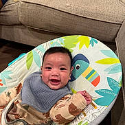 Arlo joined the competition — help win amazing prizes! baby, smiling, child, baby_rocker, seat, face, indoor, clothing, bib, happy, furniture, couch, living_room, pattern, colorful, toy, infant, person, cute, comfort
