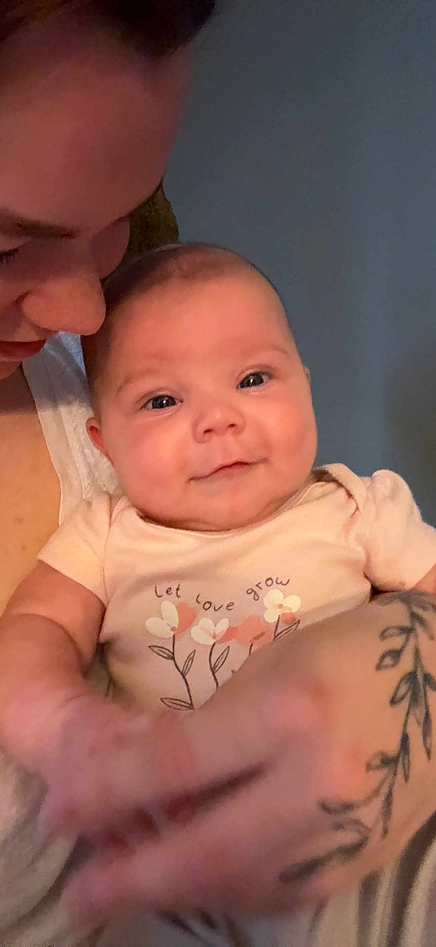 Ryker is registered to the contest to win money with this photo: baby, infant, smile, face, person, tattoo, arm, clothing, onesie, flower, text, love, holding, affection, portrait, skin, adult, happy, closeup, indoor