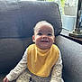 baby, bright, child, cozy, cute, furniture, gray_couch, happy, home_decor, indoor, infant, long_sleeve_clothes, natural_light, patterned_clothes, portrait, sitting, smile, window, yellow_bib, young_child