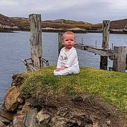 Athena joined the competition — help win amazing prizes! baby, calm, child, clothing, cloudy_sky, coast, daytime, grass, infant, landscape, nature, outdoor, quiet, rocks, scenic, serious_face, shore, sitting, water, wooden_posts