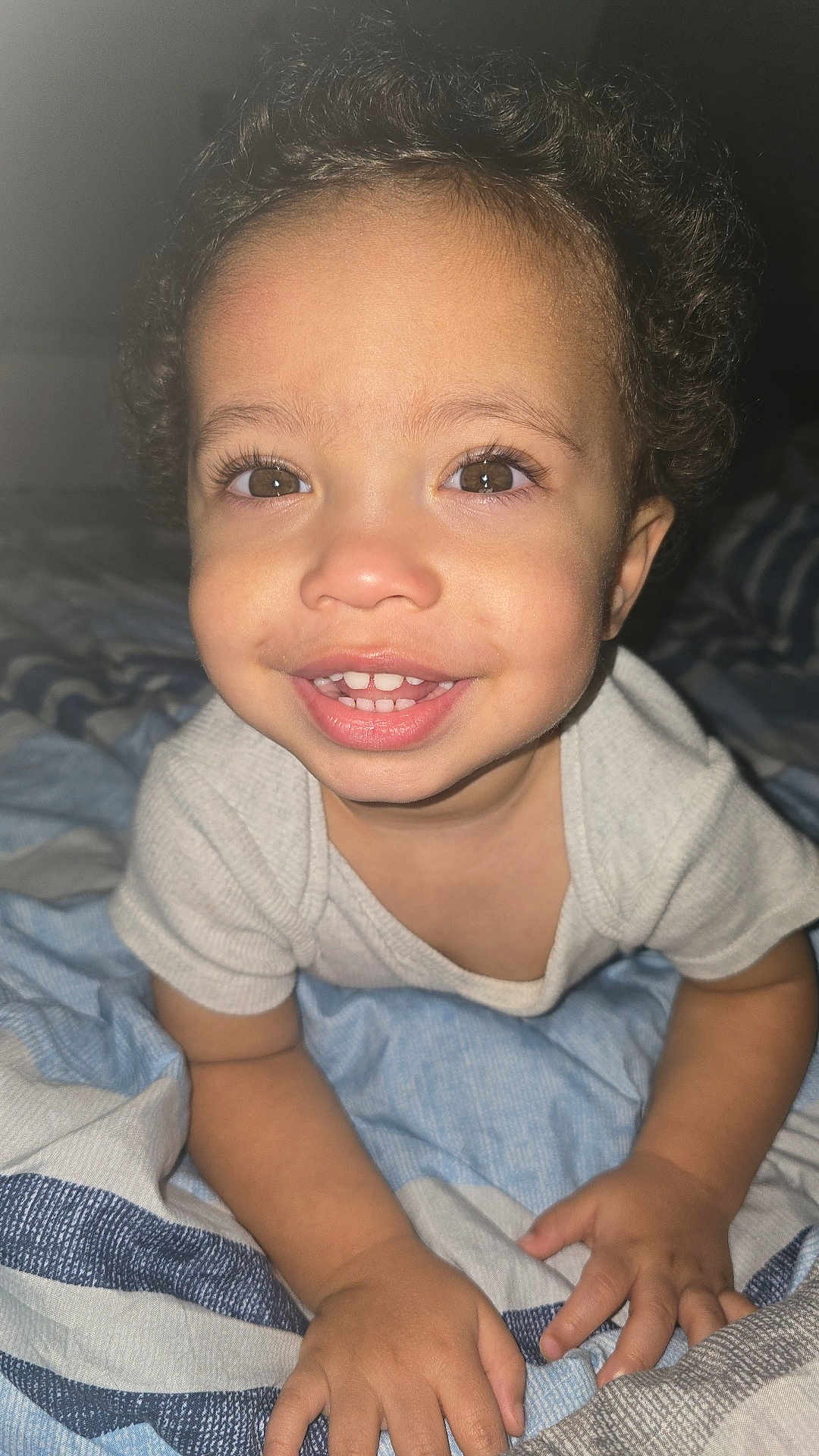 Mathias is registered to the contest to win money with this photo: toddler, child, smiling, face, eyes, hands, bed, blanket, clothing, indoor, cute, happy, crawling, person, infant, portrait, curly_hair, skin, baby, young_child
