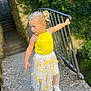 Marley a rejoint le concours — aidez-le/la à gagner de superbes lots ! child, girl, yellow_top, floral_skirt, sneakers, outdoor, stone_path, railing, nature, greenery, curly_hair, blonde_hair, earrings, daylight, casual_clothing, standing, portrait, young_child, playful, summer