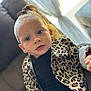 toddler, child, face, blue_eyes, leopard_print, jacket, black_clothing, couch, indoor, curious, person, earrings, hair_tied, natural_light, curtains, window, portrait, closeup, skin, furniture