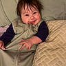 baby, smiling, sleeping_bag, pillow, bed, indoor, clothing, child, face, happy, infant, person, portrait, textile, cozy, toddler, blanket, cute, furniture, relaxing