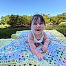 Adaline is registered to the contest to win money with this photo: baby, child, smiling, blanket, crochet, outdoor, grass, greenery, blue_sky, sunny, happy, person, infant, nature, cute, portrait, head, face, toddler, daylight