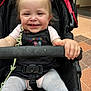 baby, child, smiling, stroller, overalls, tights, hand, face, happy, sitting, indoor, safety_belt, hair, toy, floor, tile, person, infant, clothing, playful