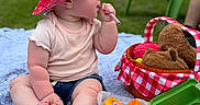 Noa is registered to the contest to win money with this photo: baby, blue_blanket, chewing, child, curious, cute, daylight, garden, grass, green_chair, outdoor, picnic, pink_shirt, plastic_toys, plush_toy, red_hat, sitting, soft_texture, summer, toy_basket