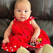 Emmalynn joined the competition — help win amazing prizes! baby, child, red_dress, polka_dots, minnie_mouse, sitting, leather_couch, white_shoes, curious, portrait, indoor, cute, infant, clothing, footwear, face, young, person, smiling, closeup