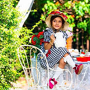 Anabia is registered to the contest to win money with this photo: chair, checkered, child, dress, flowers, garden, girl, greenery, hat, outdoor, pearls, red_bow, red_shoes, smiling, sunlight, table, tea_party, vintage_style, white_socks, white_teapot
