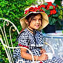 chair, checkered_pattern, child, dress, earrings, flower, flowers, garden, girl, greenery, hat, outdoor, pearl_bracelet, pearl_necklace, portrait, red_bow, smiling, teacup, vintage_style, wrought_iron