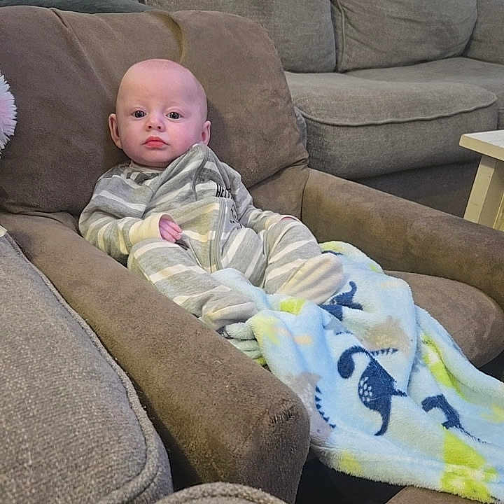 Sloan is registered to the contest to win money with this photo: baby, infant, child, sitting, armchair, sofa, couch, blanket, striped_clothing, home, living_room, furniture, portrait, indoor, face, wide_eyes, calm, cozy, textile, photography