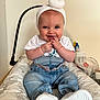 baby, blue_eyes, child, clothing, cushion, cute, denim_pants, fingers_in_mouth, happy, headwrap, indoor, infant, light_skin, patterned_cushion, person, playful, sitting, smiling, white_shirt, white_shoes