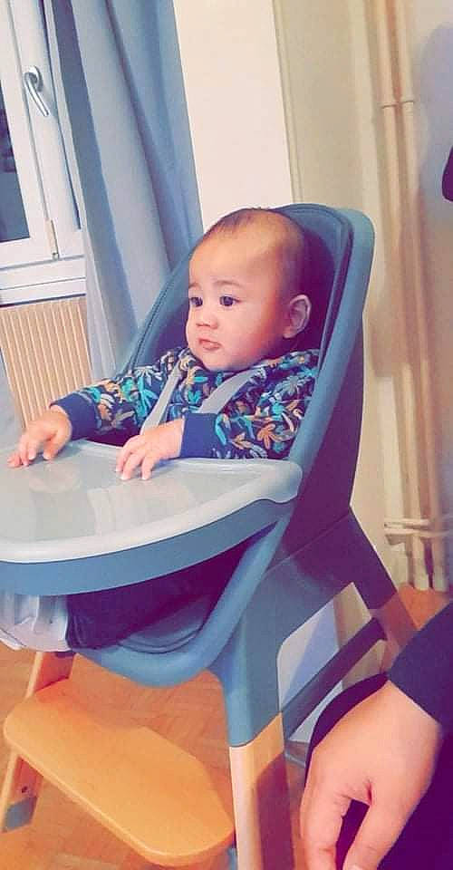 Gianni participe au concours pour gagner de l'argent avec cette photo : baby, baby_products, baby_toddler_clothing, chair, child, comfort, door, electric_blue, finger, flooring, fun, hairstyle, happy, human_leg, leisure, person, purple, sitting, table, thigh