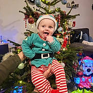 Néo participe au concours pour gagner de l'argent avec cette photo : baby, child, christmas_tree, holiday, festive_clothing, elf_costume, striped_pants, red_booties, indoor, decorations, ornaments, lights, smiling, tongue_out, person, holding_hands, cheerful, seasonal, celebration, home