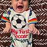 baby, infant, smiling, happy, soccer, sportswear, clothing, patterned_blanket, lying_down, cute, cheerful, child, portrait, colorful, onesie, fun, joyful, young_child, expression, celebration