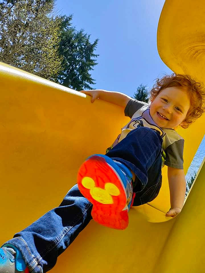 Jasper Brown is registered to the contest to win money with this photo: child, chute, clothing, fun, grass, happy, joy, leisure, orange, outdoor_play_equipment, outdoor_recreation, person, playground, playground_slide, recreation, sky, smile, sneakers, t_shirt, toddler