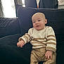 baby, child, sitting, couch, sweater, striped_clothing, pants, indoor, furniture, cozy, relaxed, window, natural_light, person, smile, cute, home, casual, infant, portrait