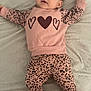 baby, barefoot, bed, blanket, child, cute, face, hearts, human, indoors, infant, leopard_print, looking, lying_down, patterned_clothing, person, pink_clothing, resting, sleepwear, young_child