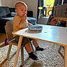 baby, child, toddler, sitting, high_chair, table, plate, snack, eating, finger_food, toys, playset, rocking_horse, living_room, couch, window, sunlight, carpet, socks, indoor