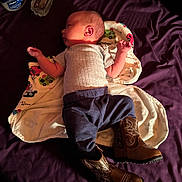 Kasen is registered to the contest to win money with this photo: baby, infant, blanket, bed, cowboy_boots, purple_bedspread, vaseline_jar, water_bottle, clothing, sleeping, lying_down, indoors, person, newborn, cute, soft_light, wooden_floor, fabric, resting, side_profile