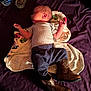 baby, infant, blanket, bed, cowboy_boots, purple_bedspread, vaseline_jar, water_bottle, clothing, sleeping, lying_down, indoors, person, newborn, cute, soft_light, wooden_floor, fabric, resting, side_profile