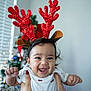 baby, child, reindeer_antlers, christmas_tree, holiday, festive, smiling, happy, hands, white_shirt, indoors, decoration, celebration, red, sparkly, person, cute, face, joyful, holiday_season