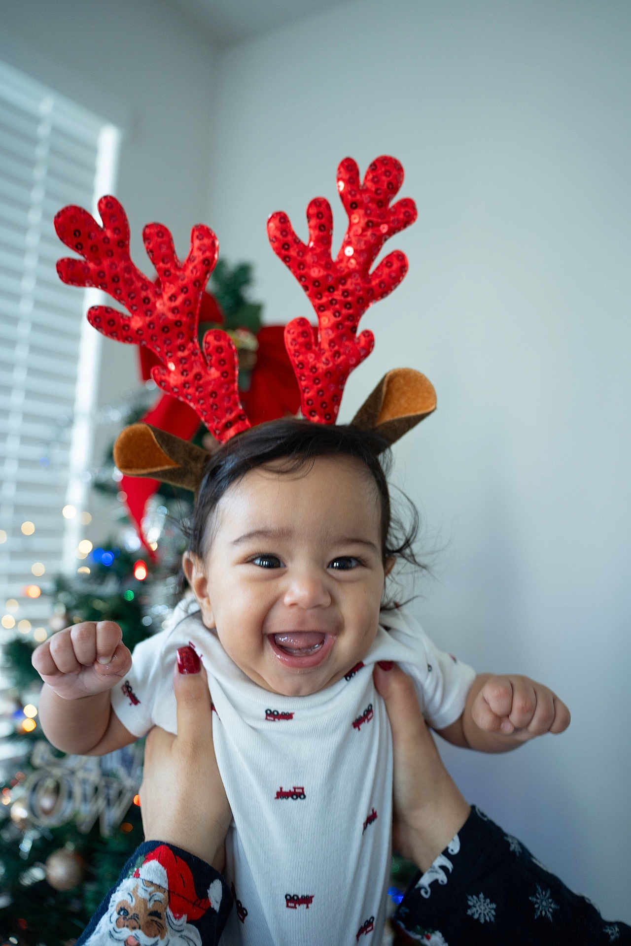 Ridhaan joined the competition — help win amazing prizes! baby, child, reindeer_antlers, christmas_tree, holiday, festive, smiling, happy, hands, white_shirt, indoors, decoration, celebration, red, sparkly, person, cute, face, joyful, holiday_season
