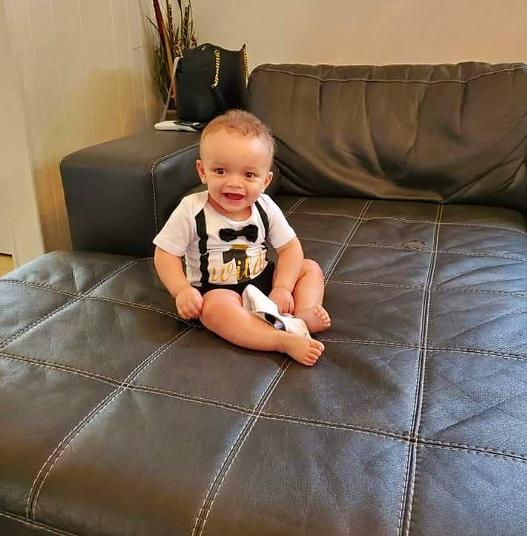 Jaxon is registered to the contest to win money with this photo: baby, baby_toddler_clothing, comfort, couch, finger, floor, flooring, furniture, hardwood, houseplant, joy, knee, leg, living_room, mammal, person, product, sleeve, smile, thigh