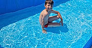 Thiméo a rejoint le concours — aidez-le/la à gagner de superbes lots ! backyard, blue, boy, child, fence, hand, happy, outdoor, pool, recreation, reflection, ripples, sitting, skin, smile, summer, sunlight, swimming_pool, swimwear, water