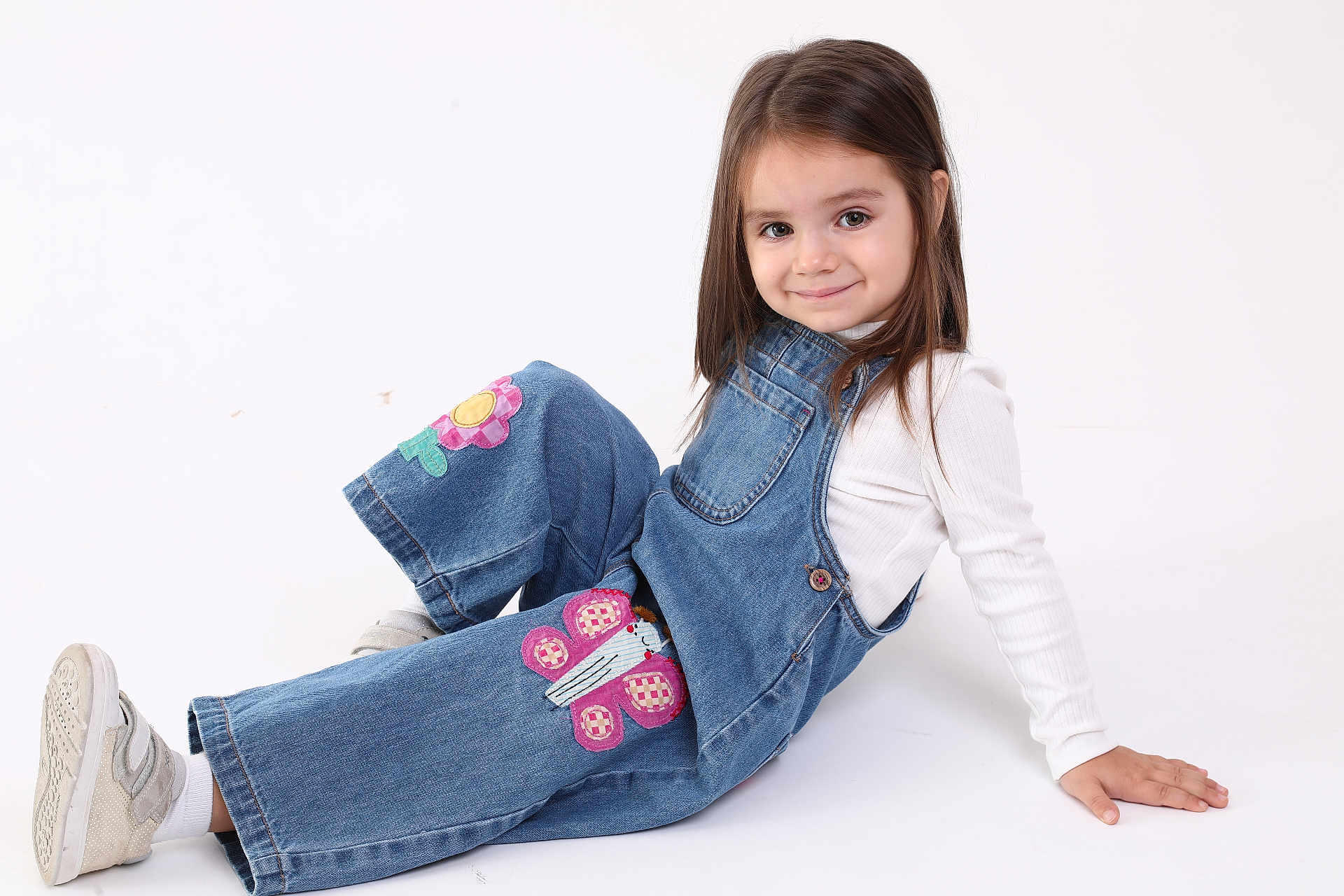 Sofia is registered to the contest to win money with this photo: child, girl, smile, denim_overalls, flower_patch, butterfly_patch, white_shirt, sneakers, long_hair, studio, pose, cute, casual_clothing, happy, fashion, portrait, young, sitting, playful, innocent