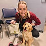 woman, certificate, golden_retriever, puppy, dog, indoor, training, smiling, leash, chair, floor, casual_clothing, happy, pet, person, white_shoes, black_pants, blonde_hair, animal, pet_training