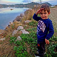 Matthias participe au concours pour gagner de l'argent avec cette photo : blue_sweatshirt, boy, casual_clothing, child, cloudy_sky, daylight, grass, greenery, lake, nature, outdoor, plants, portrait, rocks, salute, scenic, shoes, smile, standing, water