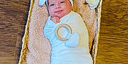 Camila is registered to the contest to win money with this photo: adorable, baby, basket, blanket, child, cute, flower, headband, indoor, infant, newborn, peaceful, person, portrait, resting, sleeping, soft_texture, swaddle, wooden_floor, wrapped