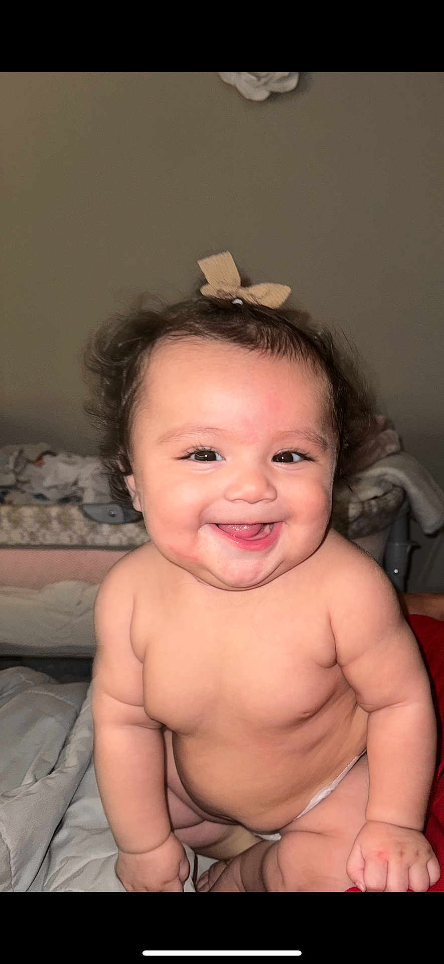Camila joined the competition — help win amazing prizes! baby, smiling, curly_hair, bow, cheeks, diaper, skin, happy, cute, infant, child, indoor, bed, blanket, bassinet, person, face, portrait, chubby, sitting