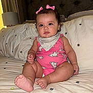 Camila is registered to the contest to win money with this photo: baby, bed, blanket, bows, child, cozy, curly_hair, cute, expression, face, feet, hand, headboard, indoor, infant, nursery, pink_clothing, portrait, sitting, soft_light