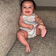 Camila is registered to the contest to win money with this photo: baby, cheerful, child, couch, cute, face, feet, hair, hands, happy, indoor, infant, onesie, plush, portrait, relaxed, sitting, skin, smiling, striped_clothing