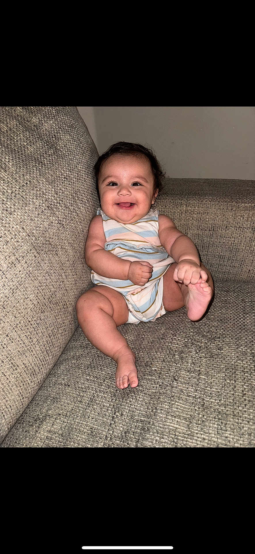 Camila is registered to the contest to win money with this photo: baby, cheerful, child, couch, cute, face, feet, hair, hands, happy, indoor, infant, onesie, plush, portrait, relaxed, sitting, skin, smiling, striped_clothing