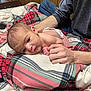 baby, infant, hands, blanket, plaid, diaper, bed, wood_paneling, person, skin, comfort, resting, indoor, young_child, support, casual_clothing, blue_jeans, long_sleeve_shirt, closeup, curious