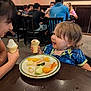 child, toddler, ice_cream, plate, fruit, table, restaurant, people, happy, smile, food, indoor, clothing, curly_hair, conversation, dining, chair, family, casual, meal