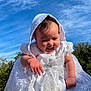 Emilia joined the competition — help win amazing prizes! baby, christening_gown, white_dress, lace, sequins, smiling, infant, outdoor, blue_sky, sunlight, happy, cute, portrait, child, celebration, hood, hand, nature, greenery, fabric