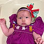 baby, child, purple_dress, embroidered_cats, headband, bow, infant, cute, chubby_cheeks, curious, lying_down, cream_background, short_hair, wide_eyes, clothing, person, portrait, indoor, hands, face
