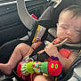 Emilia is registered to the contest to win money with this photo: baby, car_seat, sleeping, spoon, plush_toy, caterpillar_toy, infant, child, seatbelt, car_interior, clothing, hand, face, head, legs, toy, resting, cute, soft_toy, nap