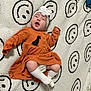 baby, black, blanket, child, clothing, cozy, cute, flower, happy, headband, indoor, infant, lying_down, orange_dress, portrait, small_person, smiling_face_pattern, soft_texture, white, white_socks