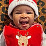 baby, smiling, red_hat, christmas_bib, reindeer, holiday, infant, cute, happy, leopard_print, patterned_background, festive, portrait, face, headwear, clothing, holiday_season, child, cheerful, indoor