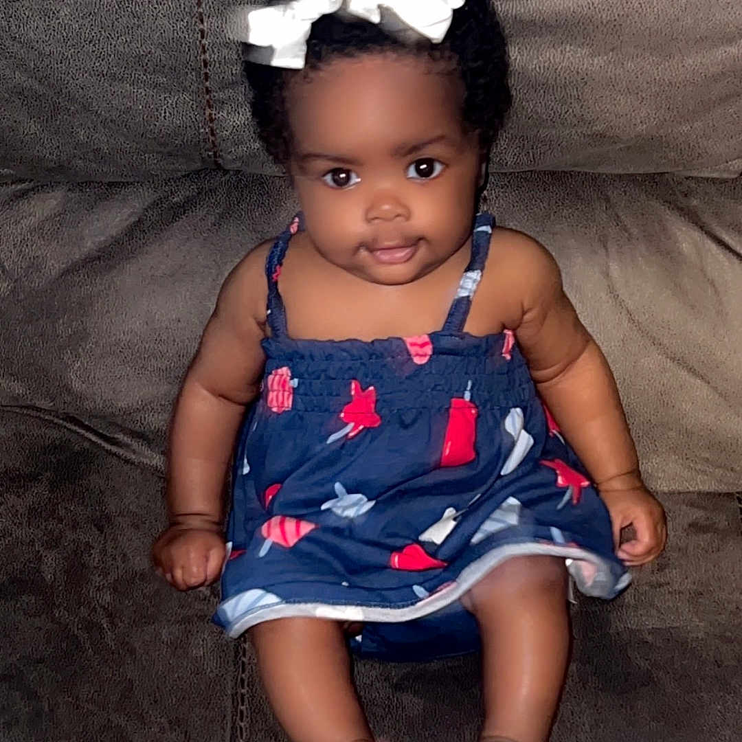 Kentoria joined the competition — help win amazing prizes! baby, barefoot, bow, brown_couch, child, comfortable, couch, curly_hair, cute, dress, face, girl, indoor, infant, navy_blue, patterned_clothing, portrait, sitting, smile, young_child