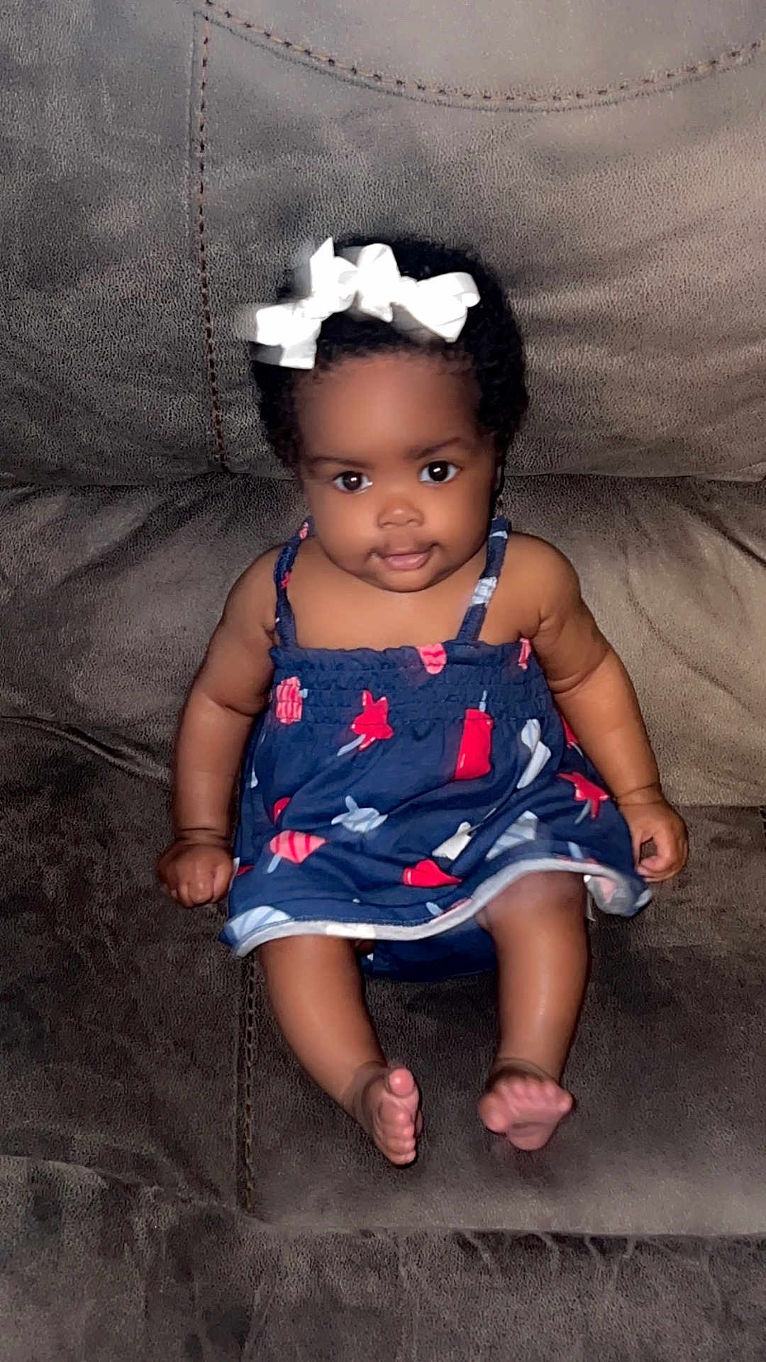 Kentoria joined the competition — help win amazing prizes! baby, barefoot, bow, brown_couch, child, comfortable, couch, curly_hair, cute, dress, face, girl, indoor, infant, navy_blue, patterned_clothing, portrait, sitting, smile, young_child
