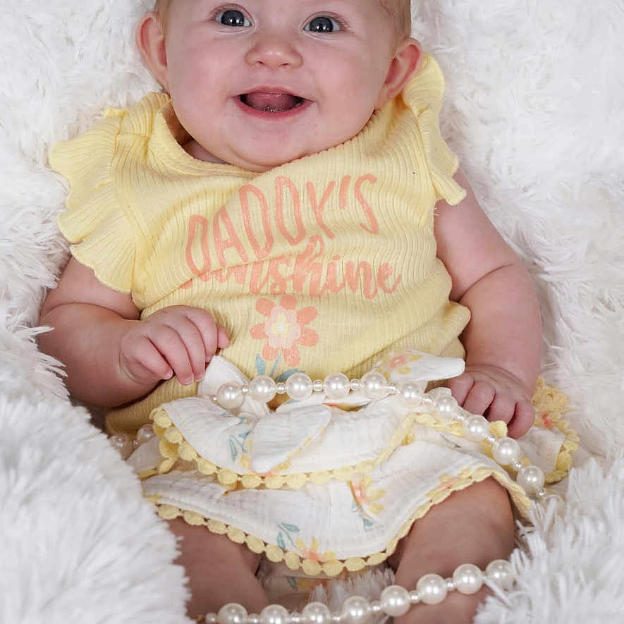 Willow is registered to the contest to win money with this photo: baby, bodypart, clothing, couch, cushion, face, finger, hand, happy, head, homedecor, laughing, mouth, newborn, pants, person, photography, portrait, sitting, smile