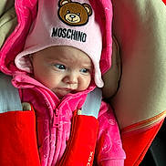 Evelyn is registered to the contest to win money with this photo: baby, child, pink, hat, hoodie, car_seat, seat_belt, red, clothing, face, person, infant, cute, expression, indoor, soft_fabric, moschino, furrowed_brow, portrait, snug